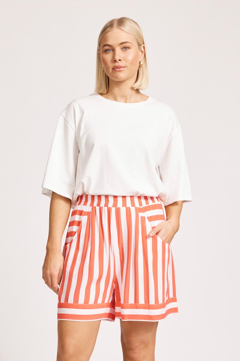 A model wearing the Treville Stripe Short in colour Coral (Red), from the front, cropped image