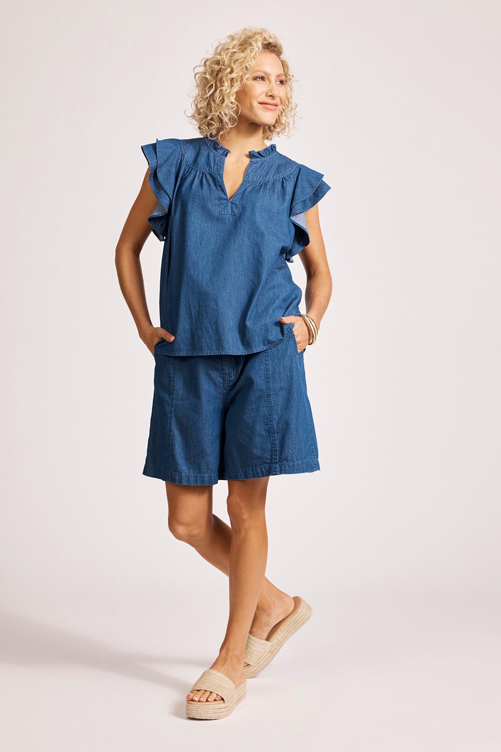 A model wearing the Melenia Denim Frill Top in colour Indigo (Blue), from the front, showing the whole outfit
