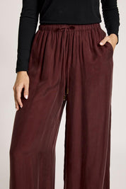 A model wearing the Calista Pant in colour Mahogany (Red), from the front, cropped image