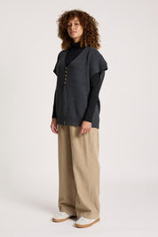 A model wearing the Berber Vest Cardigan in colour Charcoal (Black), from the front, showing the whole outfit