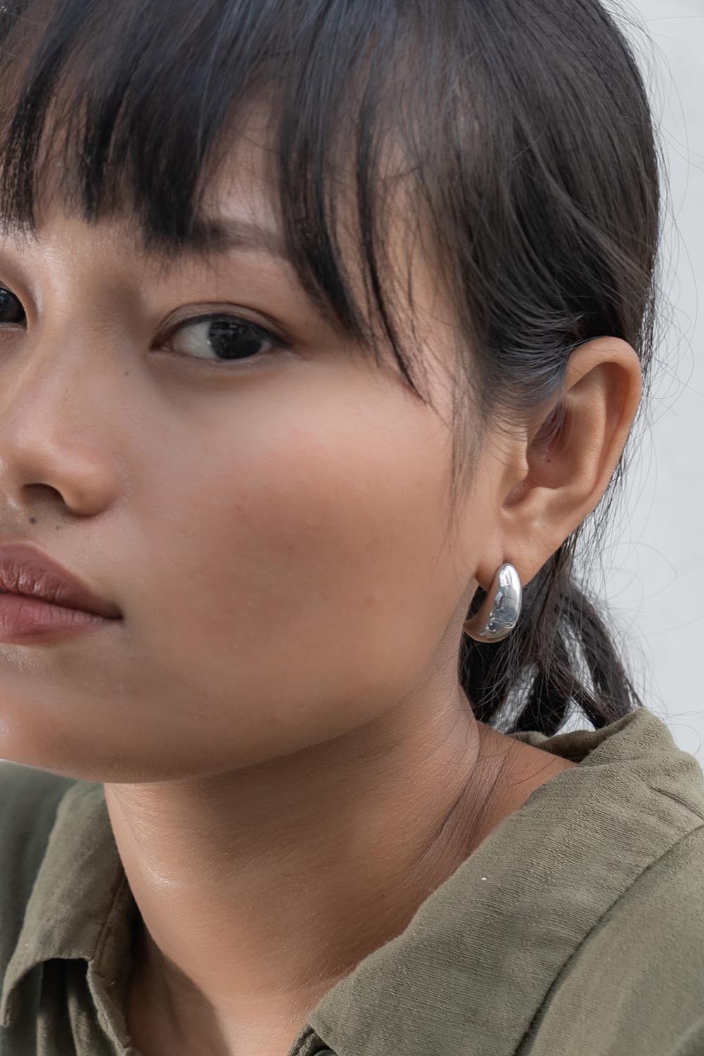 A model wearing the Love & Justice Half Hoop Earrings in colour Silver (Metallics), from the front, cropped image