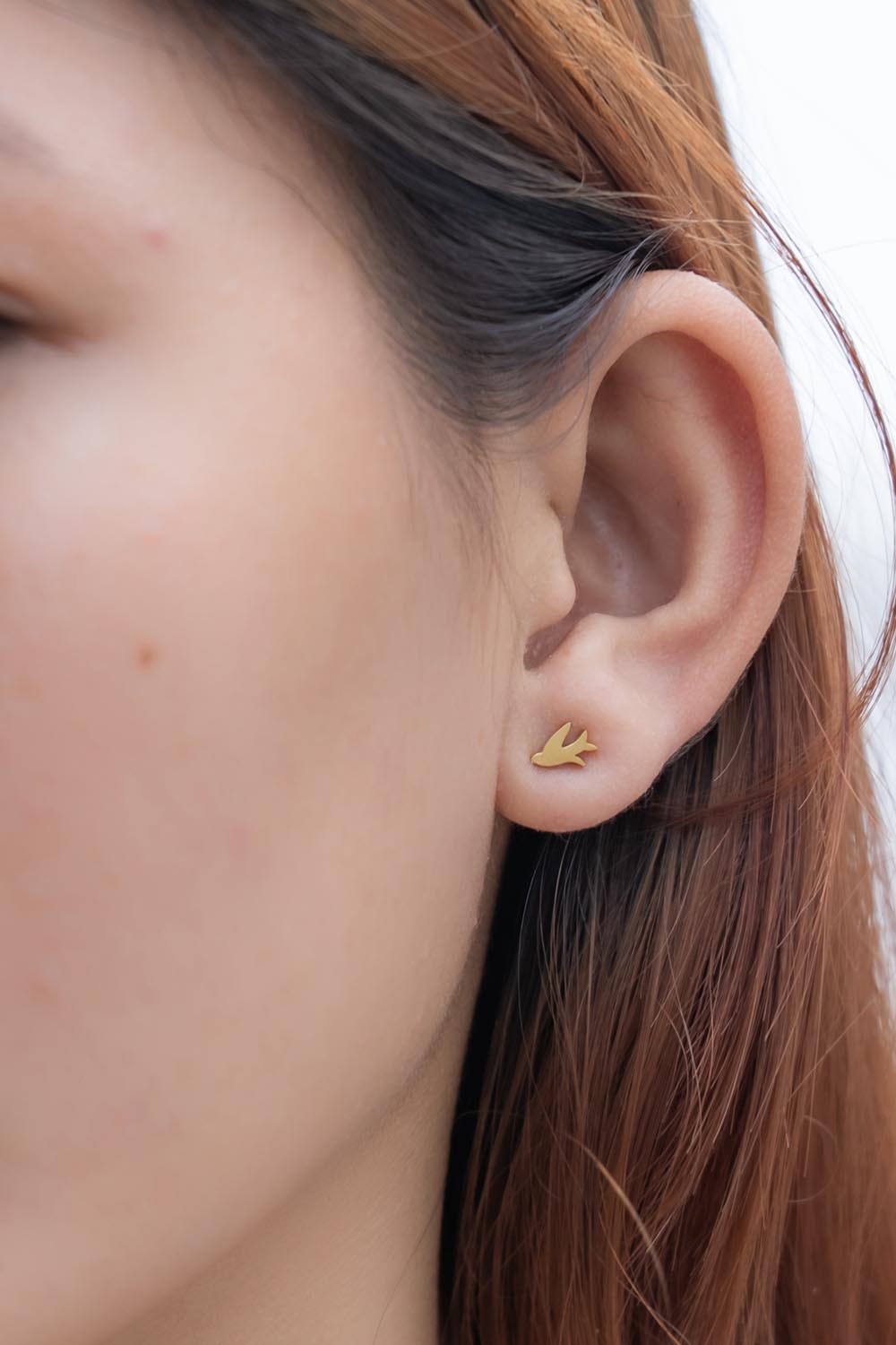 A model wearing the Song Of Freedom Post Earrings in colour Gold (Metallics), from the front, cropped image