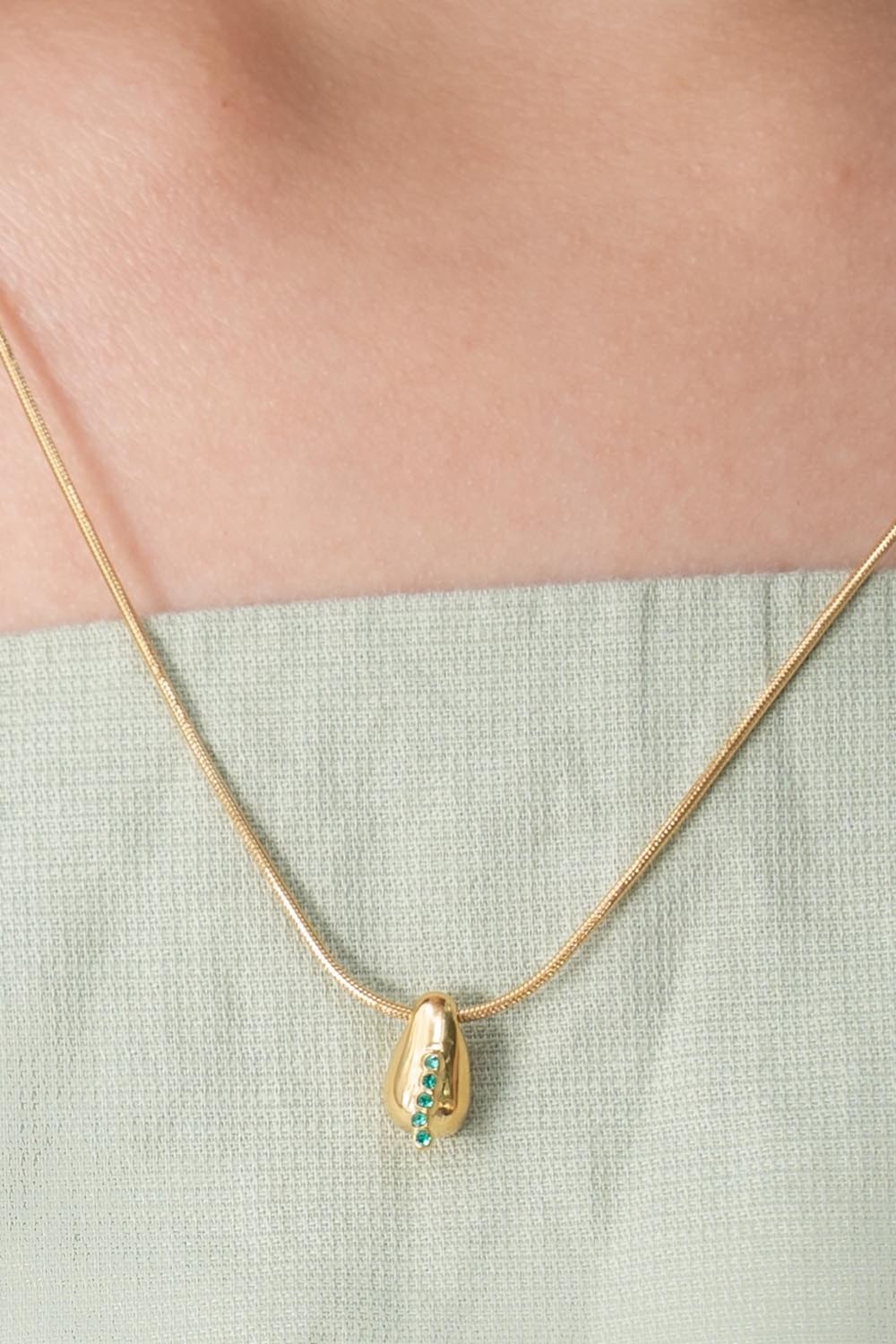 A model wearing the Radicle Drop Necklace in colour Gold (Metallics), from the front, cropped image
