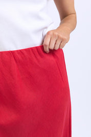 A model wearing the Eleni Linen Skirt in colour Bitterswee (Red), from the front, cropped image
