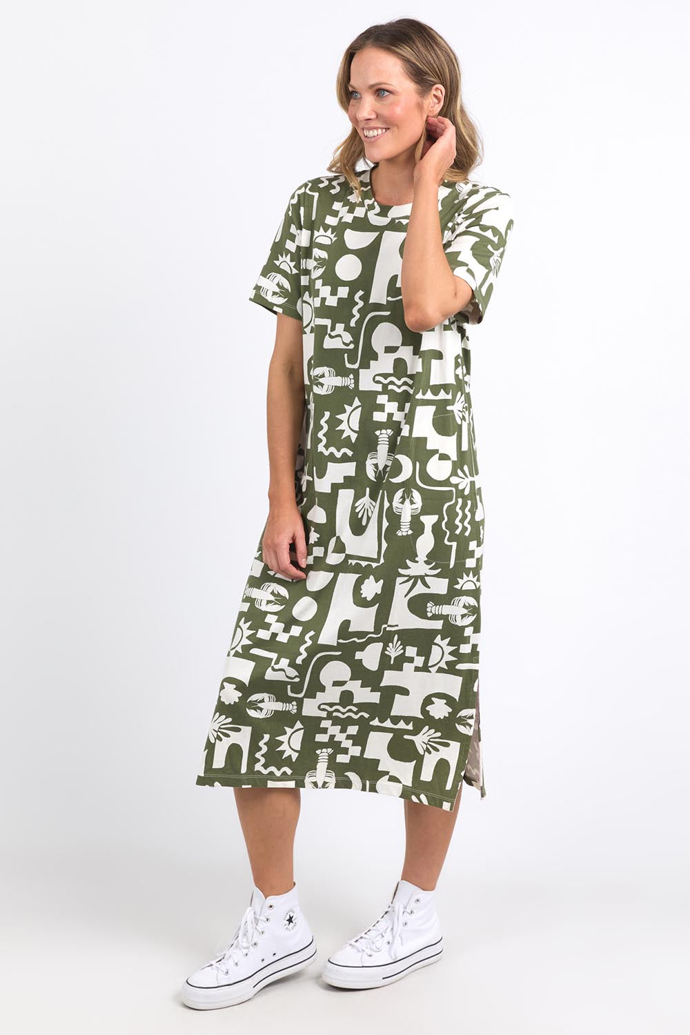A model wearing the Postcard Tee Dress Clover in colour Clover (Green), from the front, showing the whole outfit