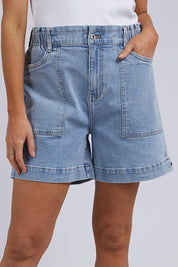 A model wearing the Atlas Denim Shorts in colour Midblue (Blue), from the front, cropped image