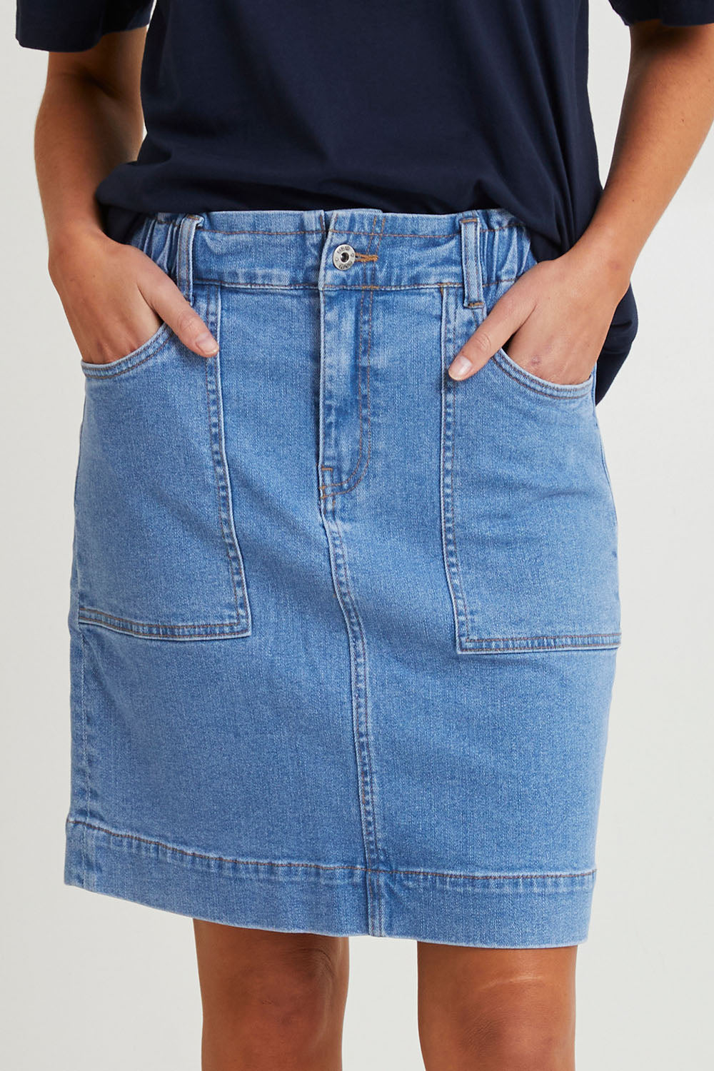 Model Madeline wearing size 10 of the Atlas Denim Skirt in colour Midblue (Blue), from the front, cropped image