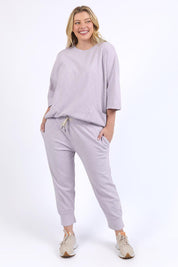 A model wearing the Fundamental Brunch Cotton Pant in colour Dustylilac (Purple), from the front, showing the whole outfit