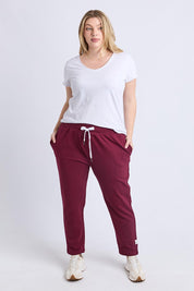 A model wearing the Fundamental Lobby Pant in colour Plum (Purple), from the front, showing the whole outfit