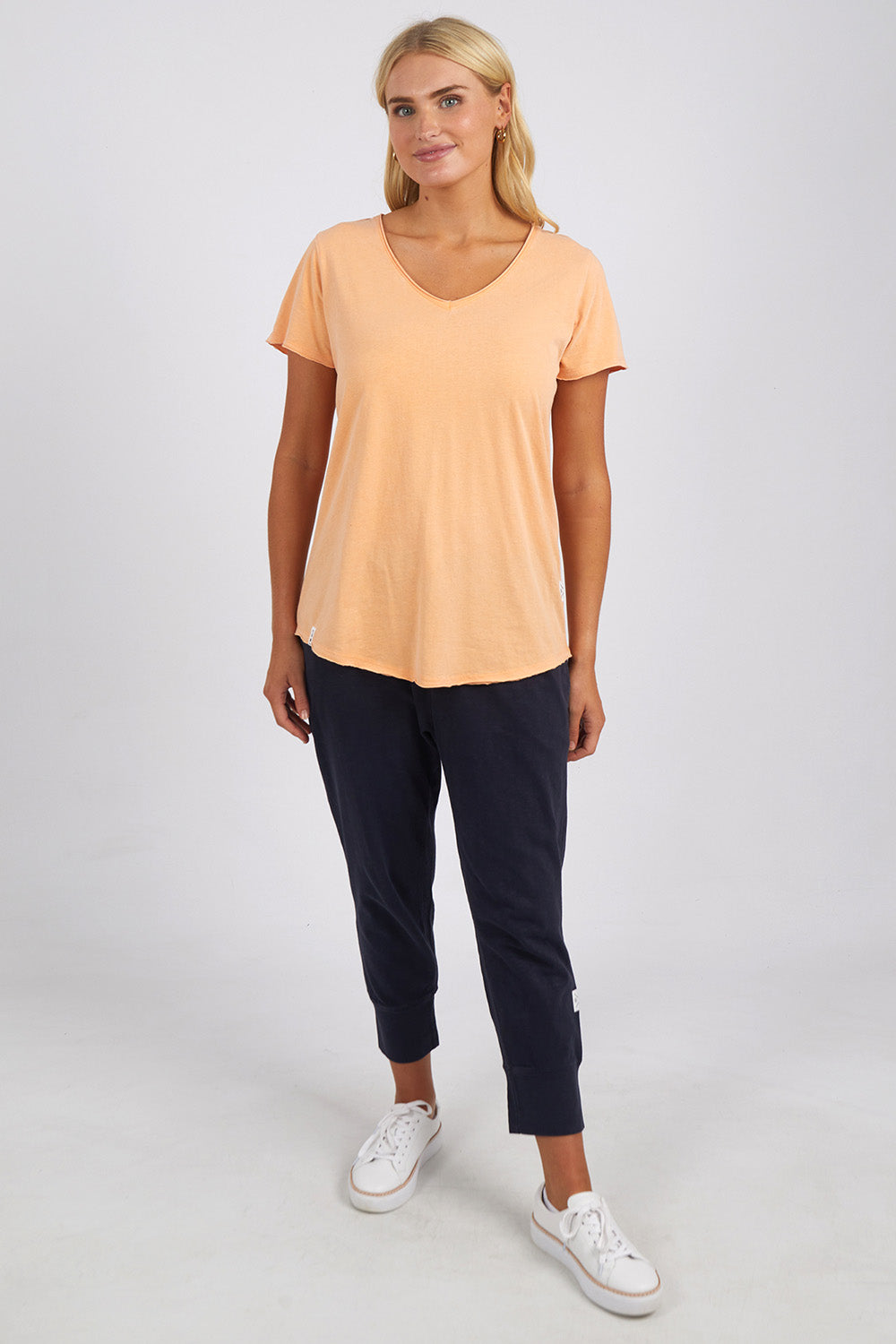 A model wearing the Fundamental Cloud Vee Tee in colour Papaya, from the front, showing the whole outfit