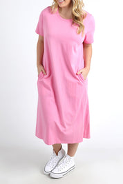 A model wearing the Fundamental Adira Dress in colour Strawberry (Pink), from the front, cropped image