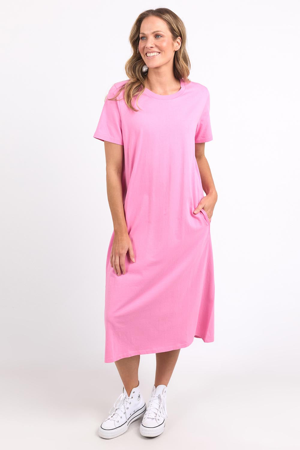 A model wearing the Fundamental Adira Dress in colour Strawberry (Pink), from the front, showing the whole outfit