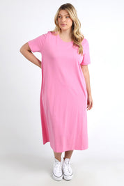 A model wearing the Fundamental Adira Dress in colour Strawberry (Pink), from the front, showing the whole outfit
