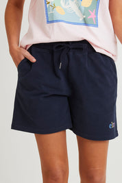 Model Madeline wearing size 10 of the Fundamental Elm Logo Short in colour Navy (Blue), from the front, cropped image