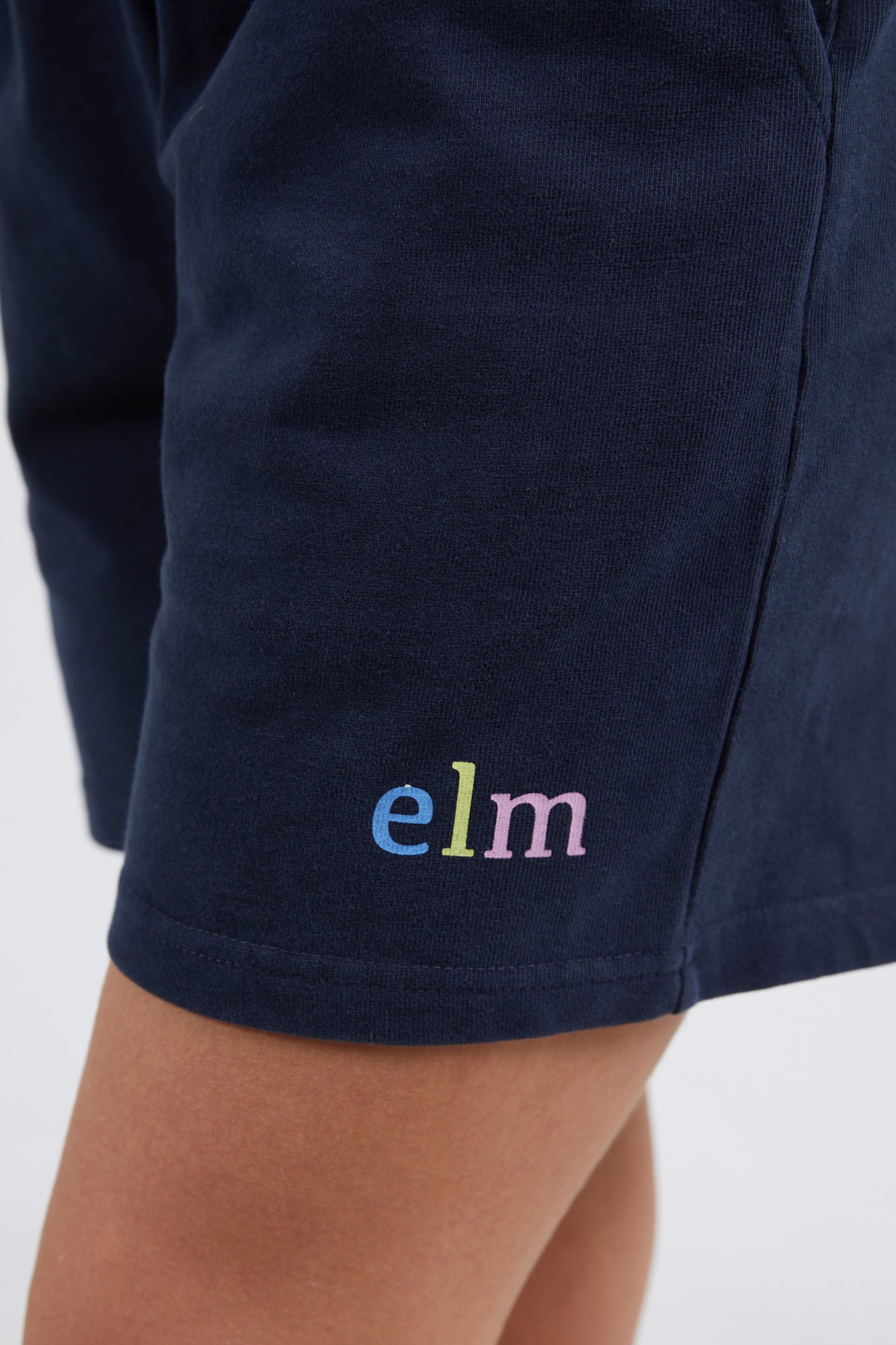 Model Madeline wearing size 10 of the Fundamental Elm Logo Short in colour Navy (Blue), from the front, cropped image