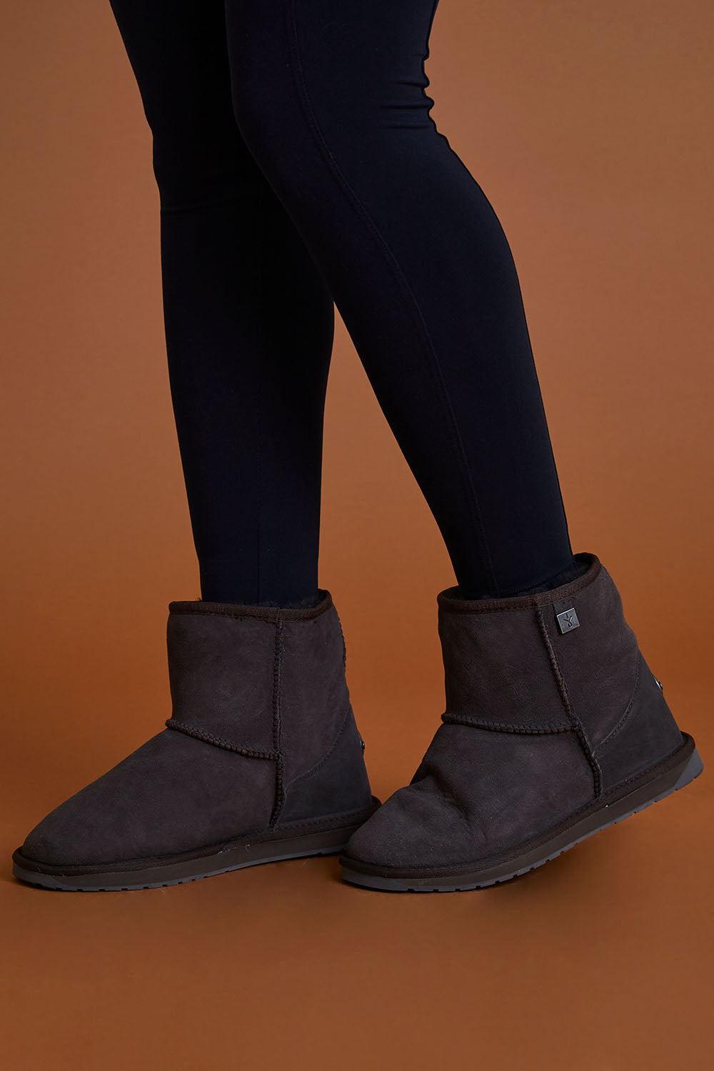 A model wearing size 9 of the Platinum Stinger Mini Ugg Boots in colour Chocolate, from the front, cropped image