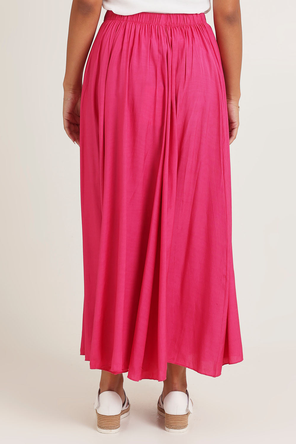 Model Ziara wearing size 10 of the Lux Crushed Maxi Skirt in colour Hotpink (Pink), from the back