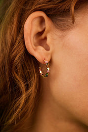 A model wearing the Coco And Tourmaline Hoop Earrings in colour Gold (Metallics), from the front, cropped image