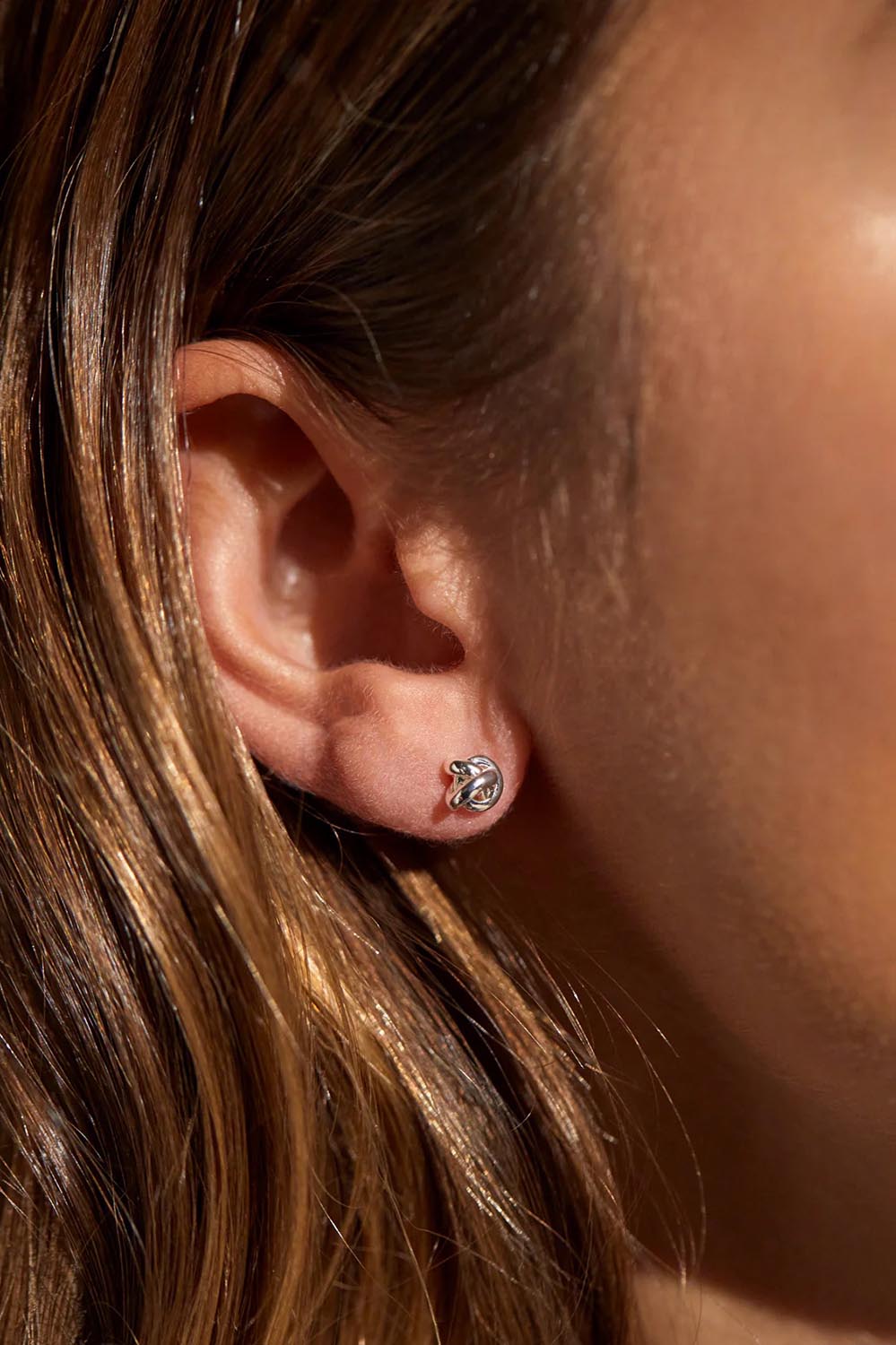 A model wearing the Knot Stud Earring in colour Silver (Metallics), from the front, cropped image