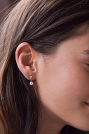A model wearing the Star & Pearl Stud Earring in colour Goldpearl (Metallics), from the front, cropped image