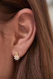 A model wearing the White Enamel Double Flower Studs in colour Whitegold (White), from the front, cropped image