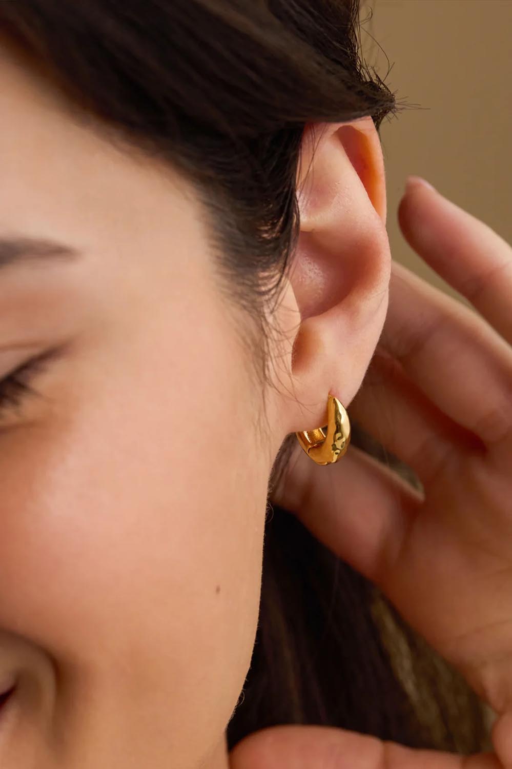 Model Genericm wearing size sample of the Hammered Huggie Hoops – Gold in colour Gold, from an angle