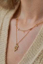 A model wearing the Tulip And Heart Necklace in colour Gold (Metallics), from the front, cropped image