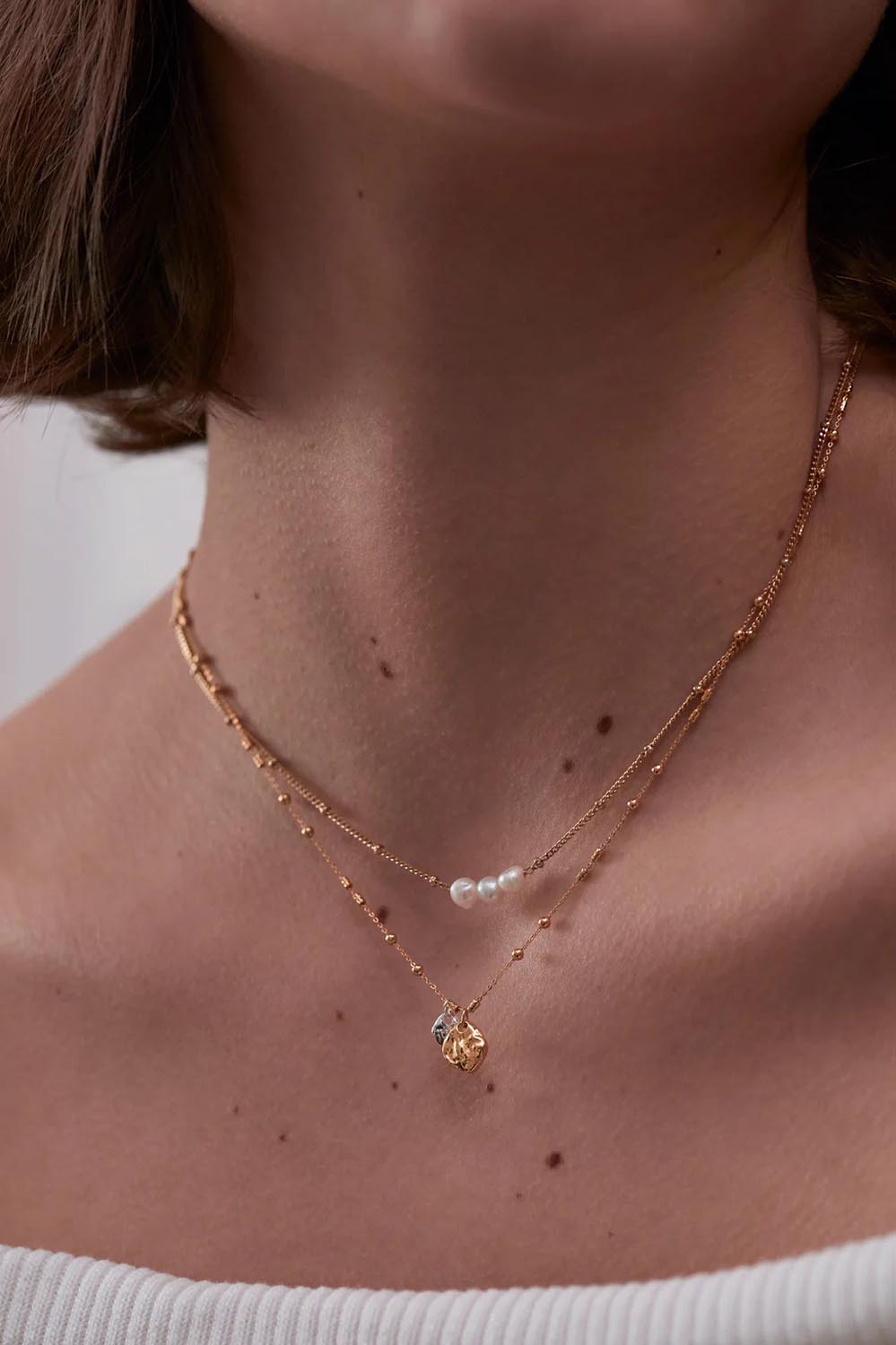 A model wearing the Beaded Chain & Molton Pebbles Necklace in colour Goldsilver (Metallics), from the front, cropped image