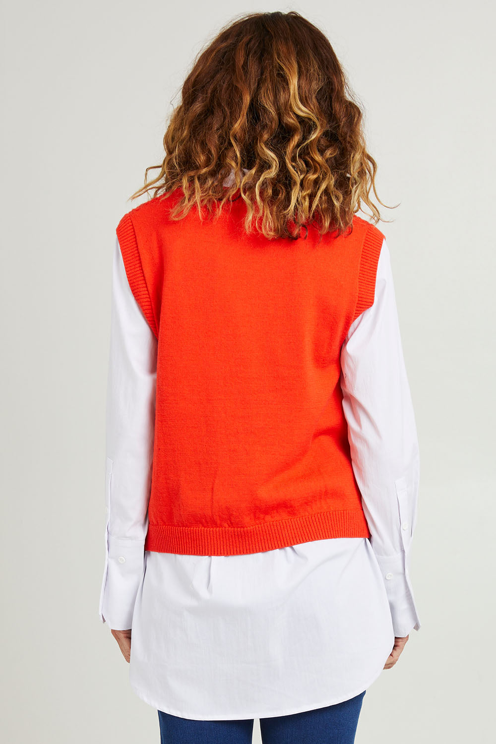 Model Emma wearing size S of the Chain Reaction Merino Vest in colour Squash, from the back