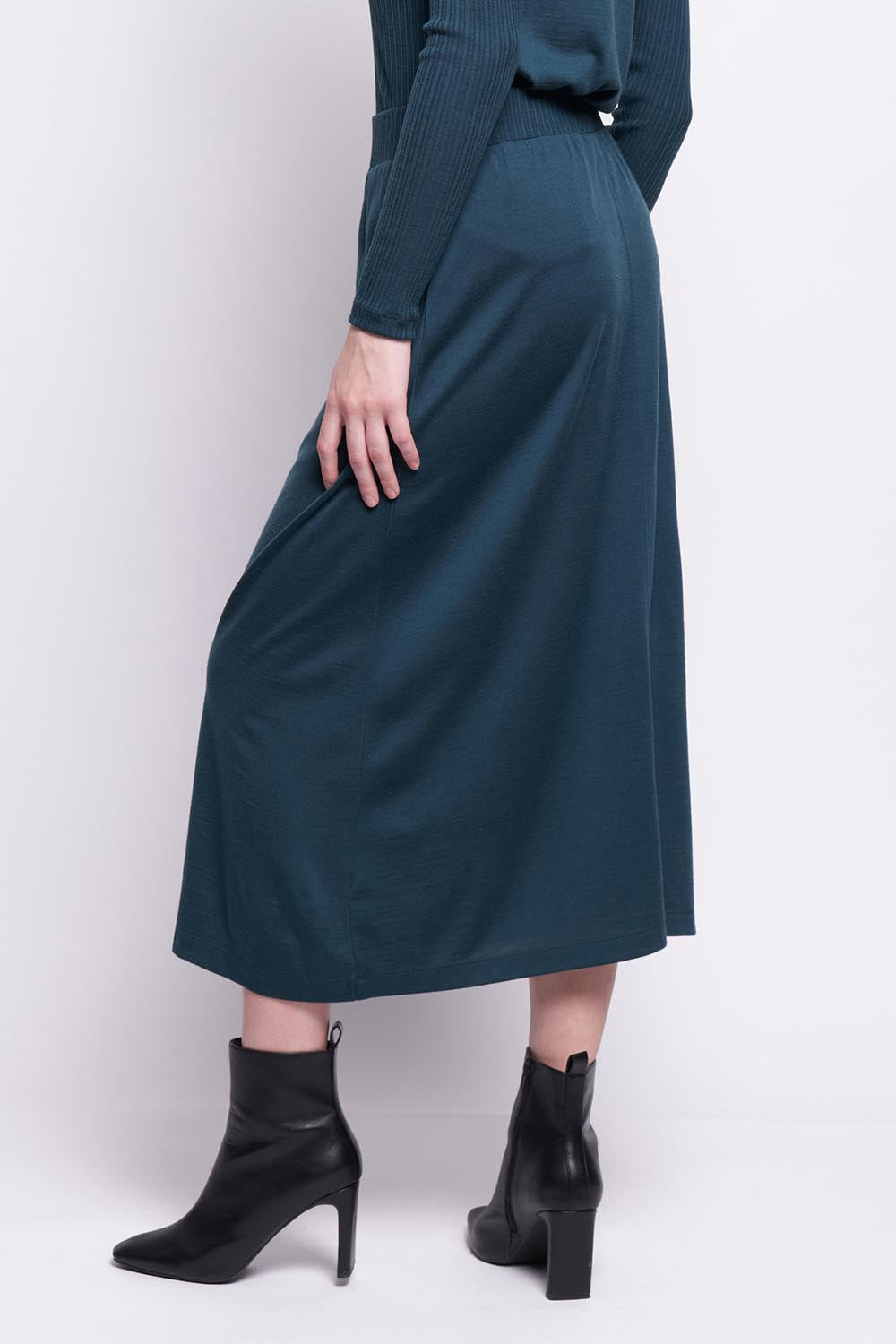 A model wearing the A Game Merino Skirt in colour Jeep (Green), from the back