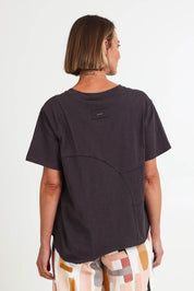 Model Riinar wearing size 10 of the Spliced And Diced Tee – Sable in colour Sable, from an angle
