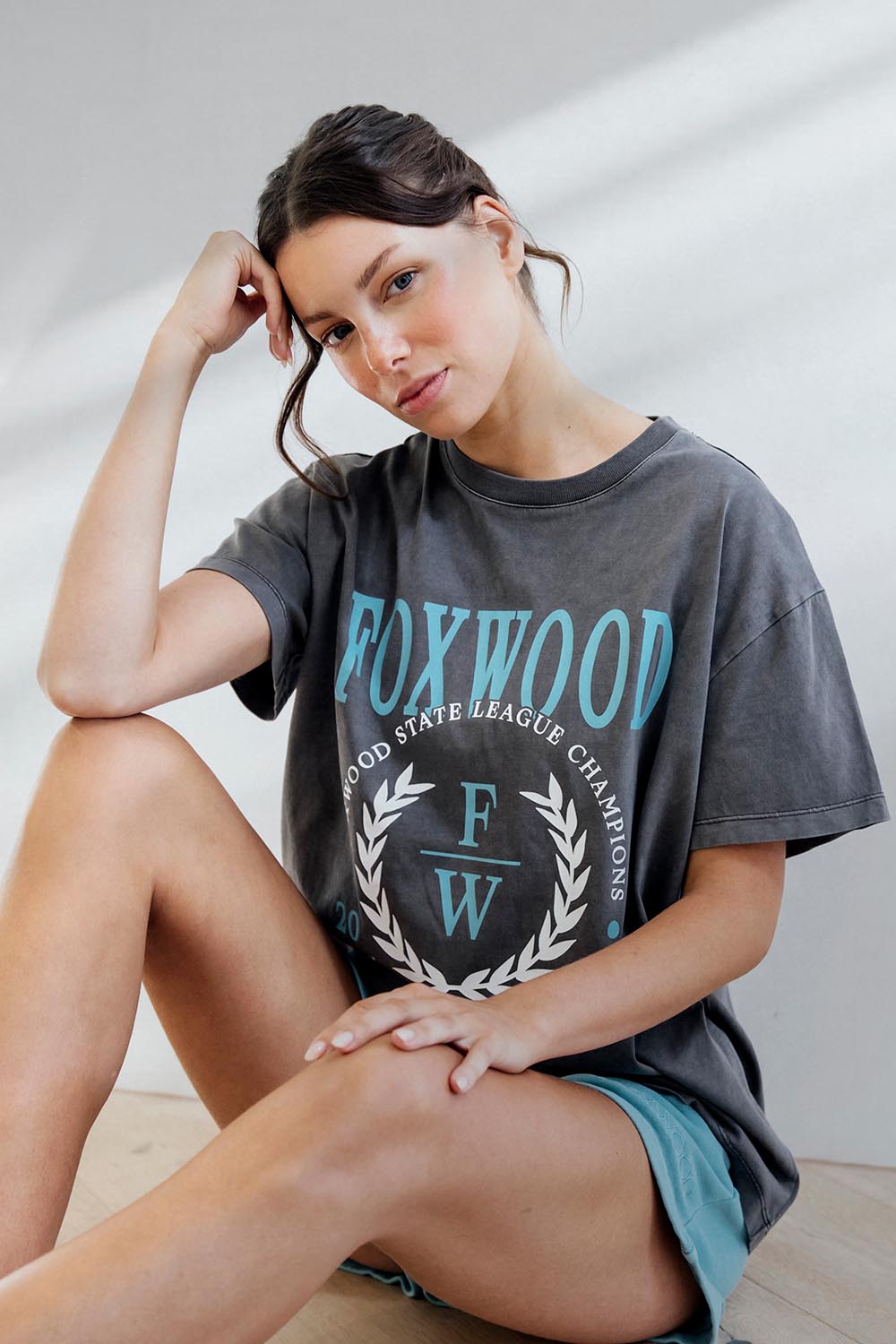 A model wearing the Leisure State League Tee in colour Iron (Grey), from the front, showing the whole outfit