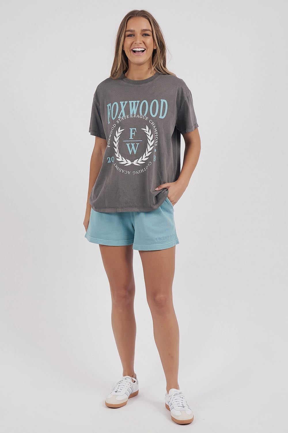 A model wearing the Leisure State League Tee in colour Iron (Grey), from the front, showing the whole outfit