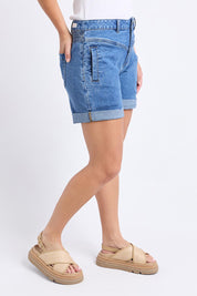 A model wearing the Elements Devi Denim Shorts in colour Midblue (Blue), from the front, cropped image