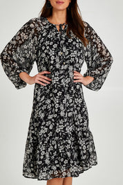 Model Madeline wearing size 10 of the Beautiful Soul Frill Hem Midi Dress in colour Monofloral (Black), from the front, cropped image