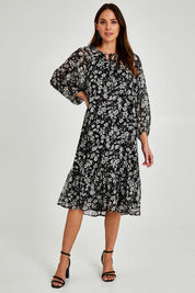 Model Madeline wearing size 10 of the Beautiful Soul Frill Hem Midi Dress in colour Monofloral (Black), from the front, showing the whole outfit