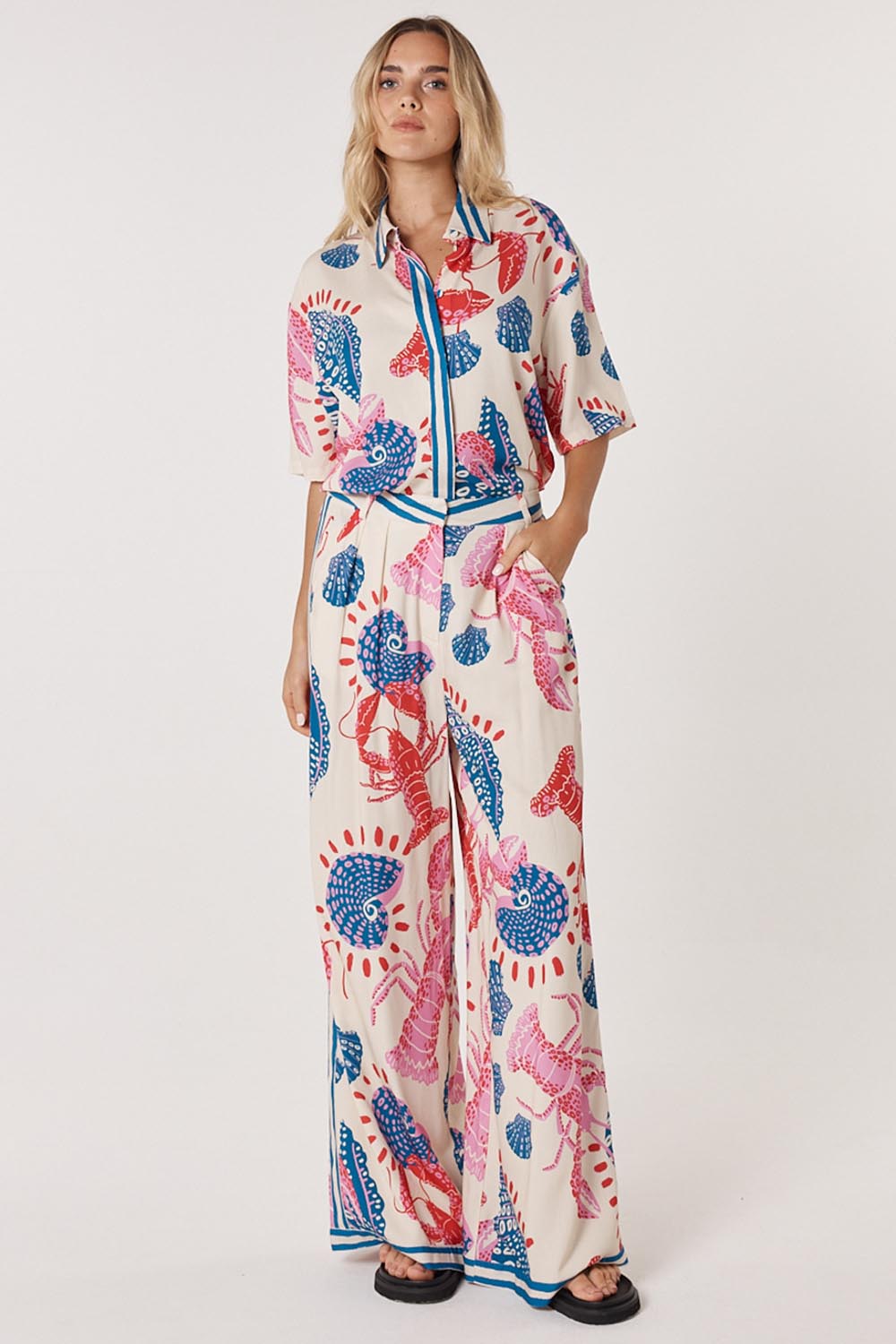 A model wearing the Soleil Pant in colour Lobster, from the front, showing the whole outfit