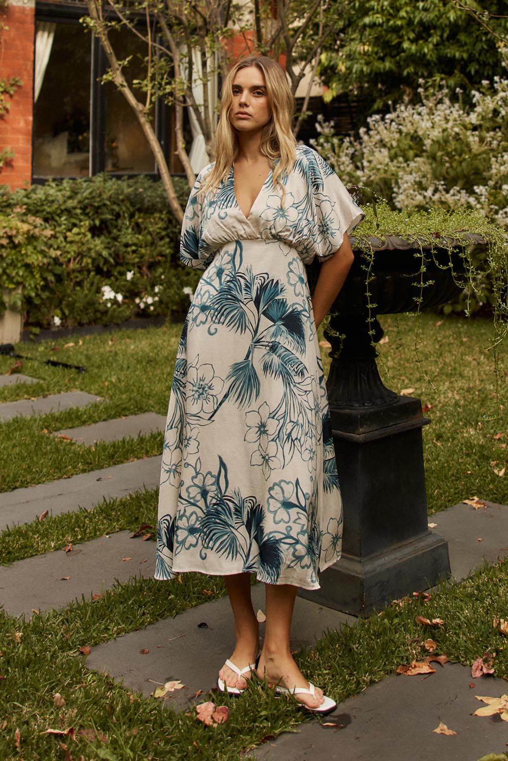 A model wearing the Solstice Palms Midi Dress in colour Palm (Blue), from the front, showing the whole outfit