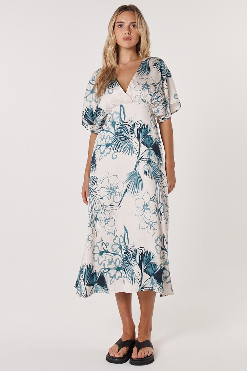 A model wearing the Solstice Palms Midi Dress in colour Palm (Blue), from the front, showing the whole outfit