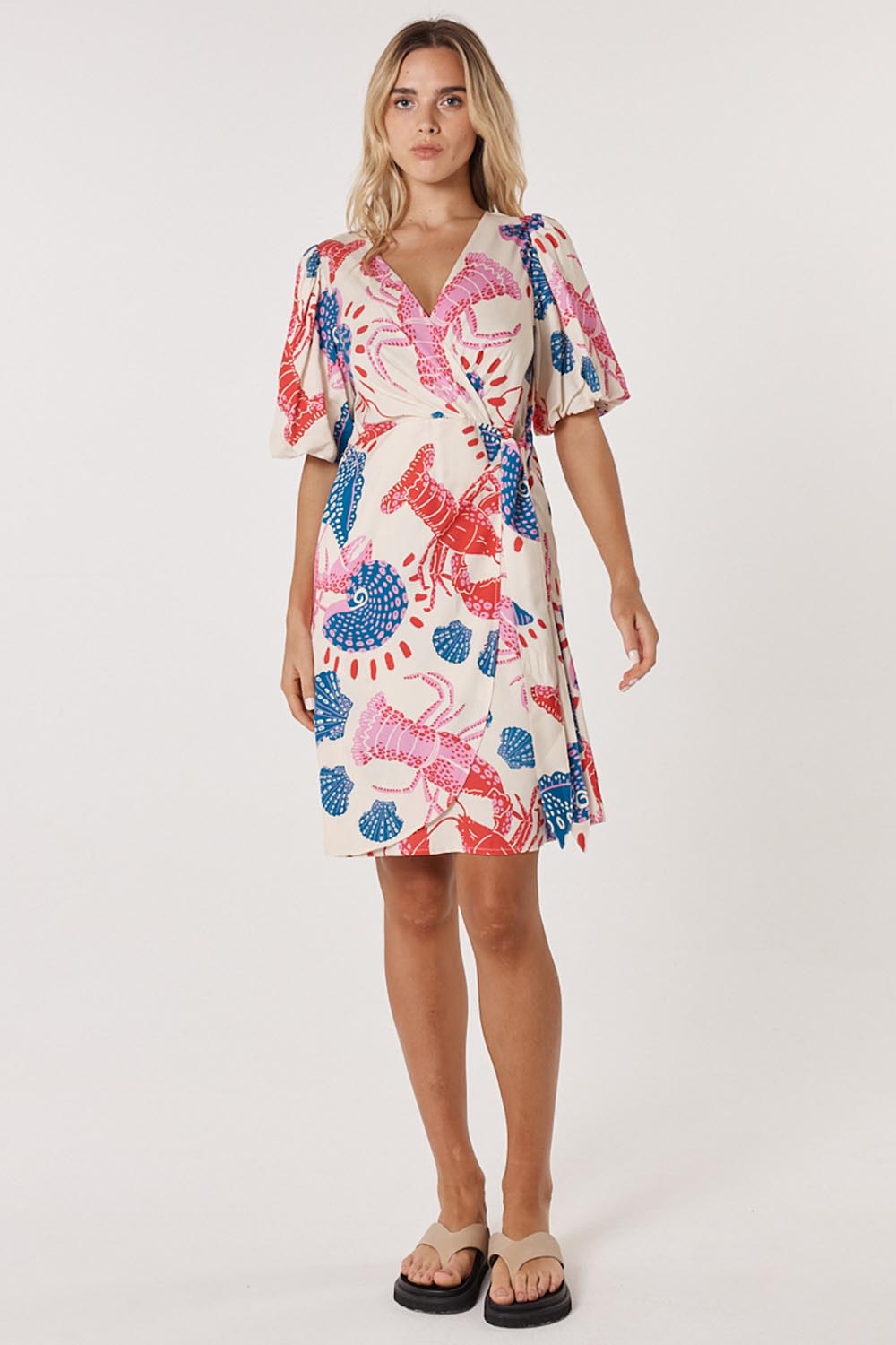 A model wearing the Soleil Wrap Dress in colour Lobster, from the front, showing the whole outfit