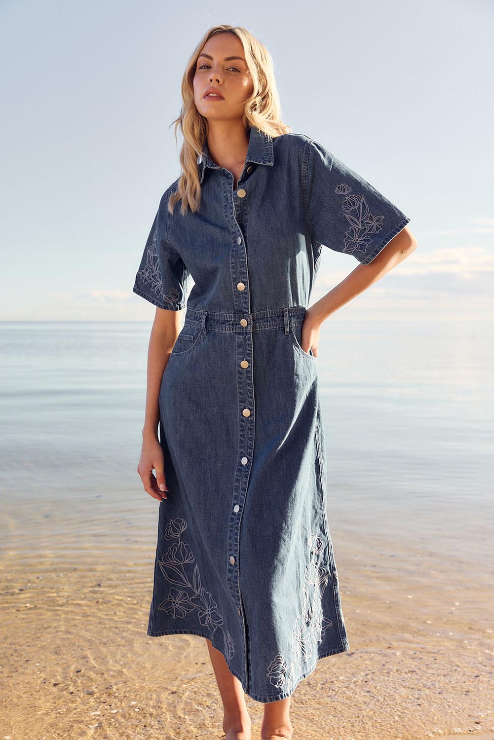 A model wearing the Sloane Embroidered Denim Dress in colour Midblue (Blue), from the front, showing the whole outfit