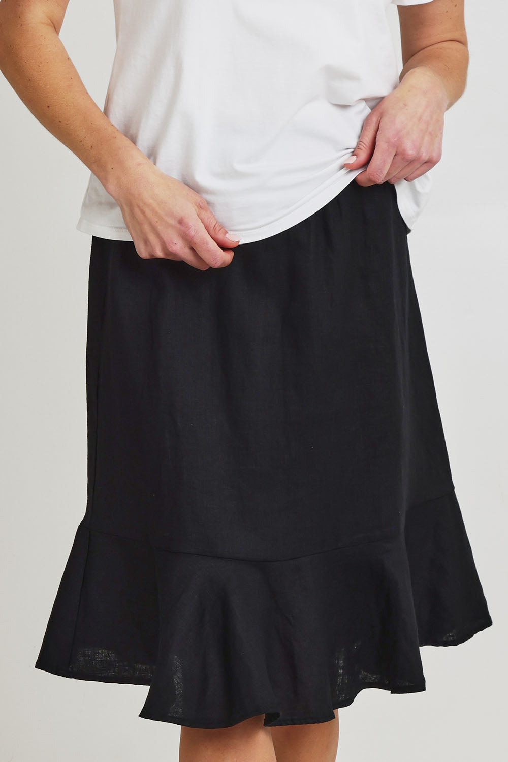 Model Olivia wearing size 10 of the Piccolo Linen Skirt in colour Black (Black), from the front, cropped image