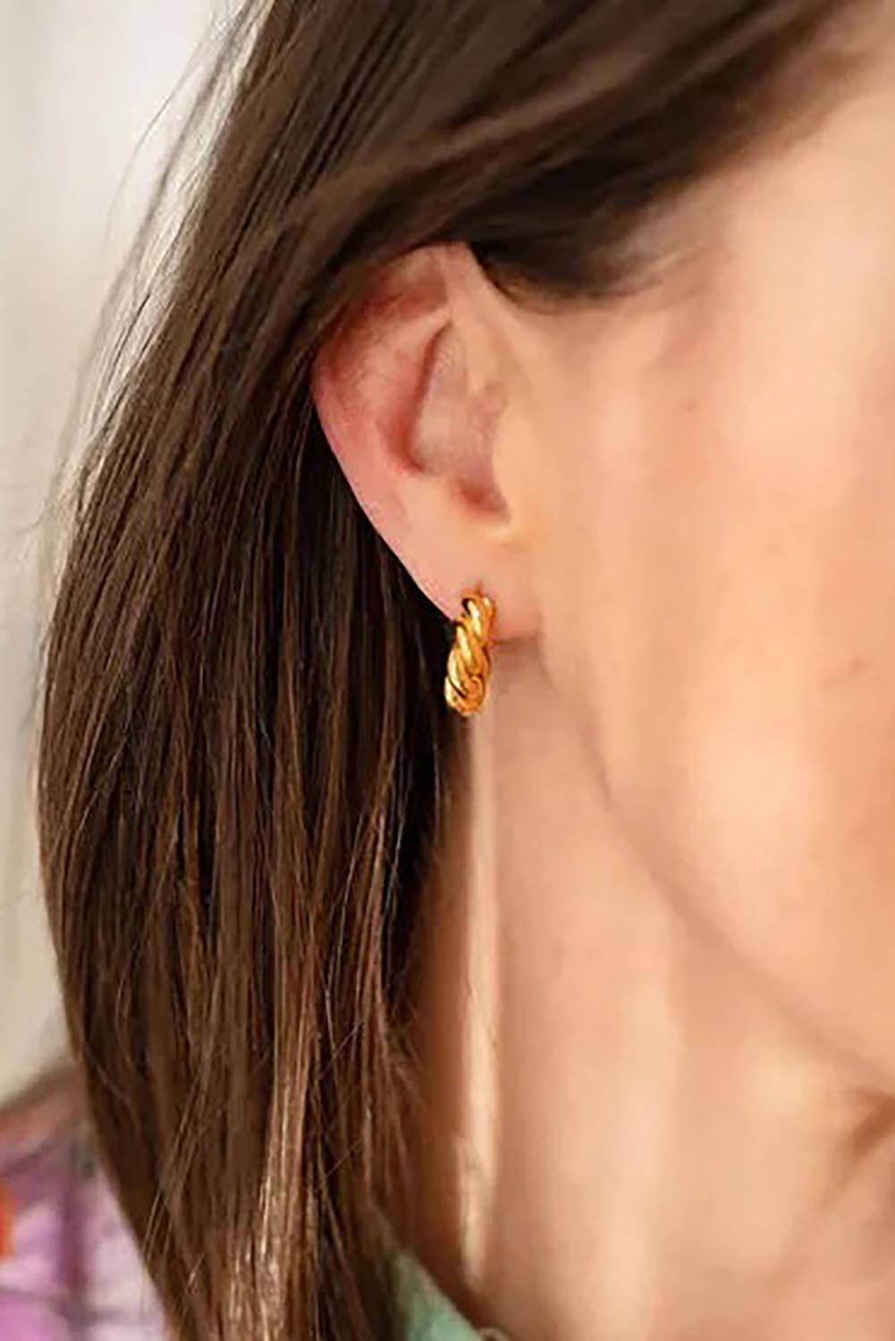 A model wearing the Audrey Twisted Hoops in colour Gold (Metallics), from the front, cropped image
