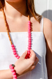 A model wearing the Mini Wood & Rock Necklace in colour Brightpink (Pink), from the front, cropped image