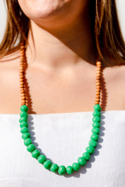 A model wearing the Mini Wood & Rock Necklace in colour Emerald (Green), from the front, cropped image