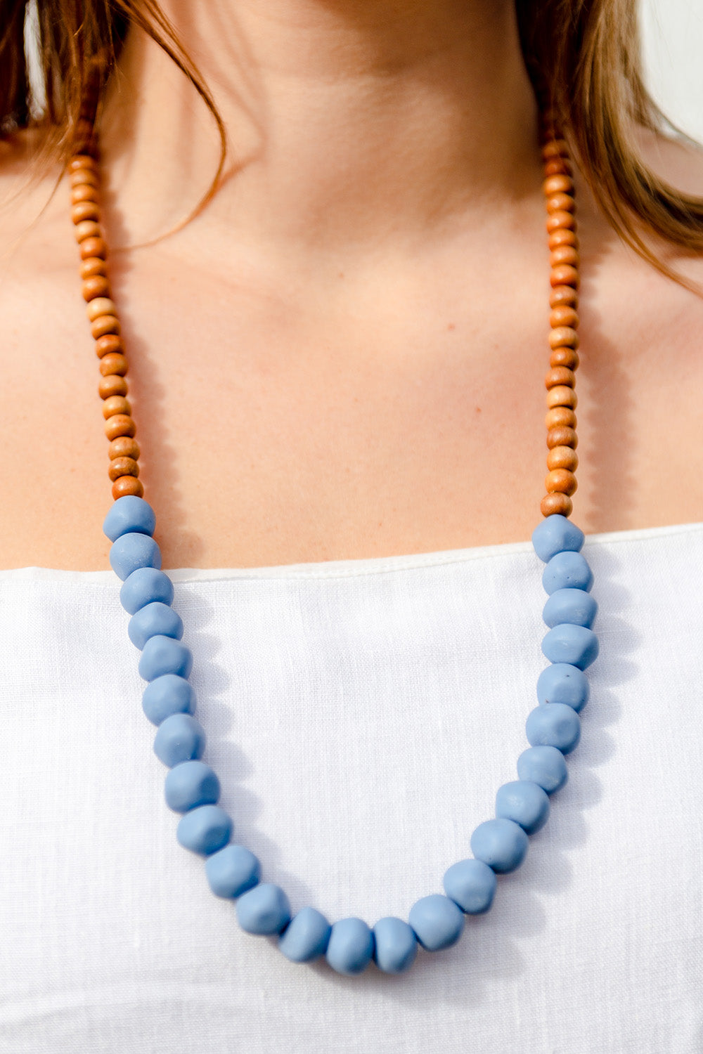 A model wearing the Mini Wood & Rock Necklace in colour Jacaranda (Blue), from the front, cropped image