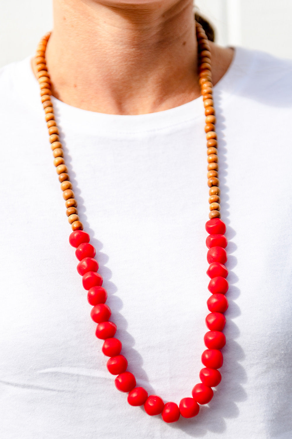 A model wearing the Mini Wood & Rock Necklace in colour Red (Red), from the front, cropped image