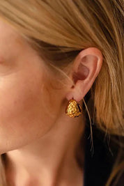 A model wearing the Mona Hammered Teardrop Hoop in colour Gold (Metallics), from the front, cropped image