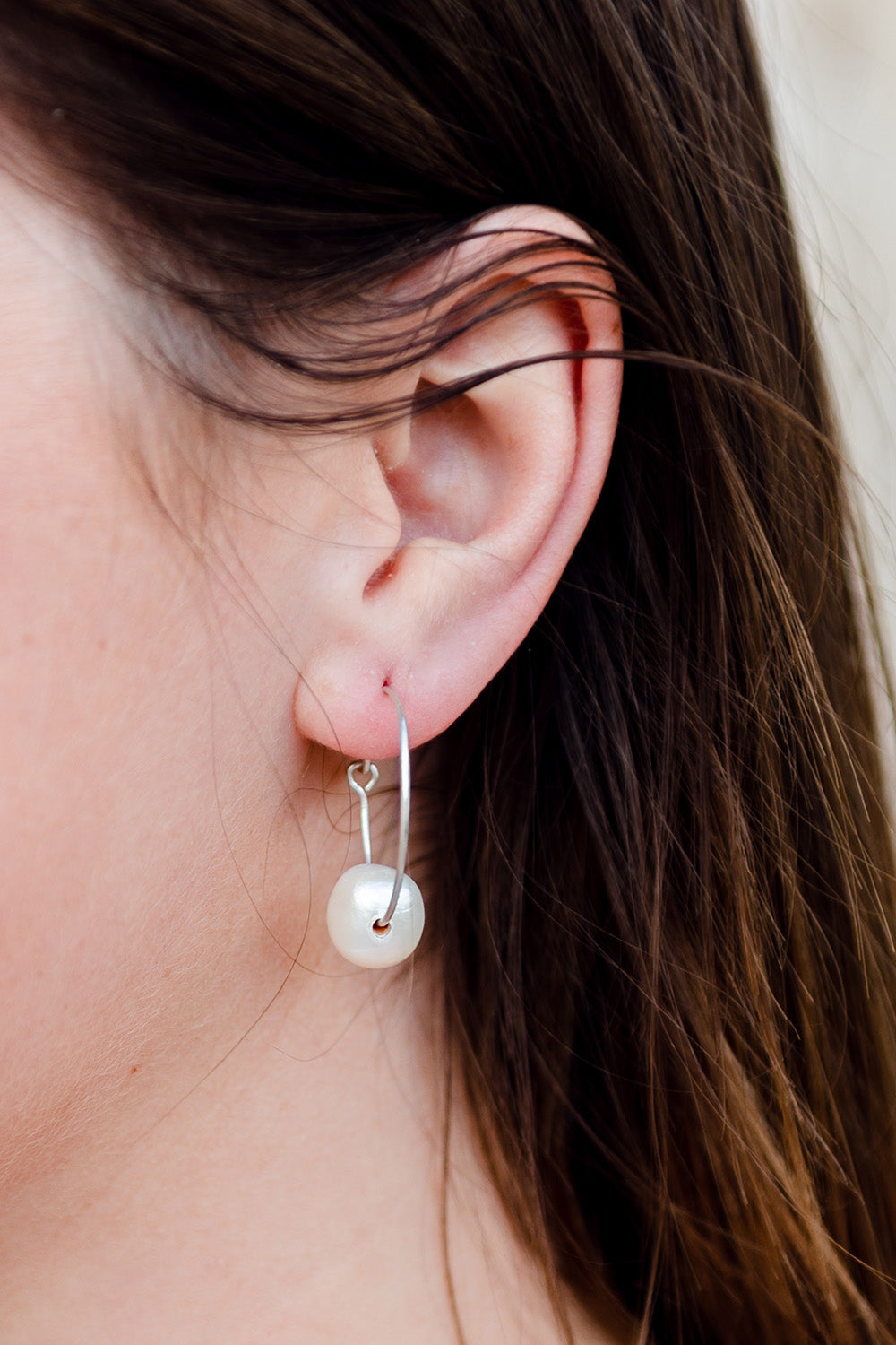A model wearing the Freshwater Single Pearl Hoop Earring in colour Silver (Metallics), from the front, cropped image