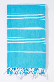 A model wearing the Hammamas Original Cotton Towel in colour Aqua (Blue), from the front, showing the whole outfit